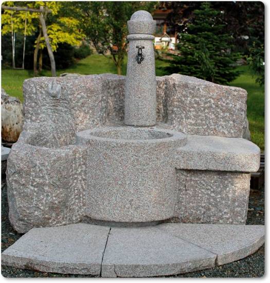 Das ist ein Granitbrunnen mit Bank und seitlichen Pflanzmulden.
