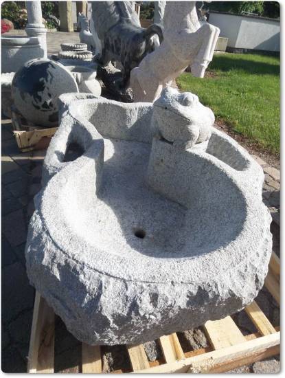 Das ist ein Springbrunnen mit einem Frosch in der Mitte. Dieser Brunnen besteht aus Granit und hat seitliche Pflanzmulden.